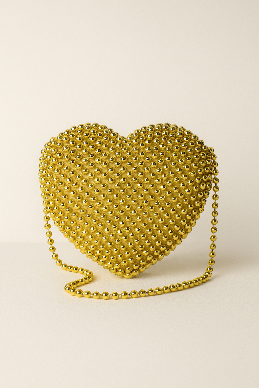 Gold heart-shaped handbag with chain strap on a beige background